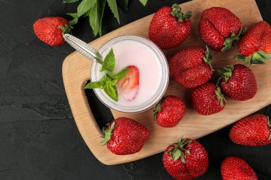 bir kavanozve taze olgun çilek ve siyah beton masa üzerinde bir nane yaprağı lezzetli çilek yoğurt. üst görünüm