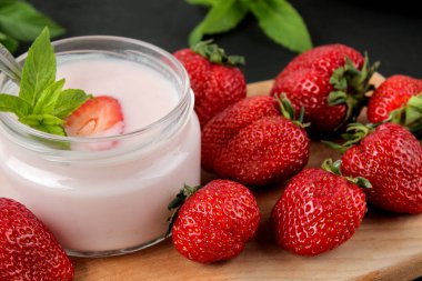 bir kavanoz ve taze olgun çilek ve siyah beton masa üzerinde bir nane yaprağı lezzetli çilek yoğurt.