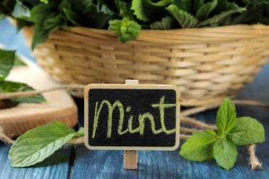 Nane. Yapraklar ve taze yeşil yabani nane dalları bir sepet ve ahşap mavi bir masa üzerinde bir yazıt ile bir işaret. Close