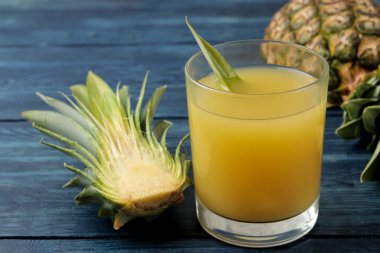 Bir bardak ananas suyu ve mavi ahşap arka plan üzerinde taze ananas parçaları. Yaz. Meyve.