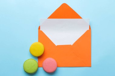 Parlak trendy açık mavi arka plan üzerinde bir yazıt antetli ve makarna kek ile turuncu zarf. üst görünüm