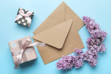 Parlak trendy açık mavi arka plan üzerinde leylak ve hediye kutusu bir sprig ile Zanaat zarf. üst görünüm