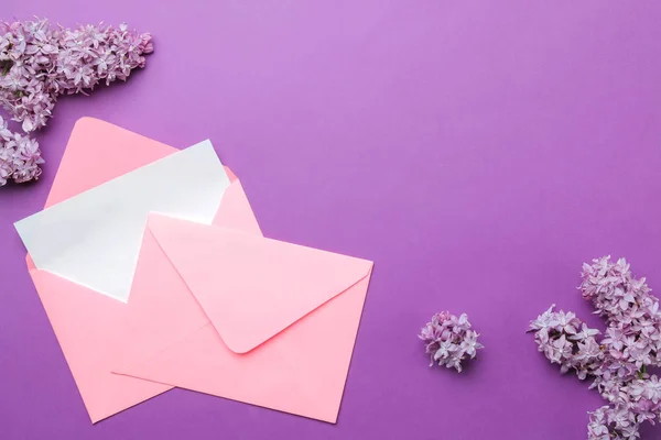 明るいトレンディなライラックの背景に碑文とライラックの小枝のための空白とピンクの封筒 トップビュー — ストック写真