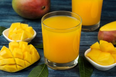 Olgun taze mango meyve ve dilimler ve mango suyu mavi ahşap bir masa üzerinde bir bardak. tropikal meyve.
