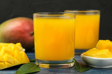 Olgun taze mango meyve ve dilimler ve mango suyu mavi ahşap bir masa üzerinde bir bardak. tropikal meyve.