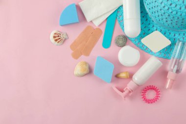 Seyahat için kozmetik ve kişisel bakım ürünleri seti ve yumuşak pembe arka plan üzerinde bir şapka. üst görünüm