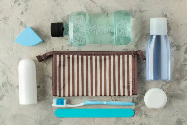 A set of cosmetics and personal care products for travel in a cosmetic bag on a light concrete background. top view. travel cosmetics