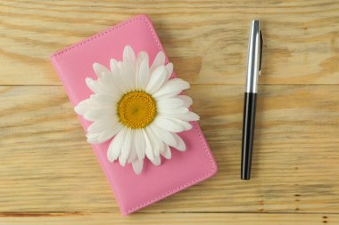 Doğal ahşap bir masa üzerinde büyük beyaz papatya çiçekler ve pembe not defteri. üst görünüm.