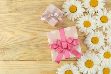Doğal ahşap bir masa üzerinde büyük beyaz papatya çiçekler ve hediye kutusu. çiçek çerçevesi. üst görünüm. metin için alan