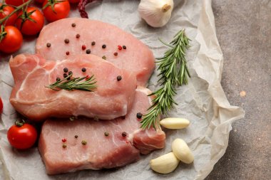 Çiğ domuz biftek, et ve pişirme için malzemeler, baharatlar, otlar ve koyu bir arka plan üzerinde sebze. üst görünüm.