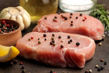 Çiğ domuz biftek, et ve pişirme için malzemeler, baharatlar, otlar ve koyu bir arka plan üzerinde sebze. Close