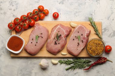 Tahtada çiğ domuz biftek, et ve pişirme için malzemeler, baharat otlar ve hafif bir arka plan üzerinde sebze. üst görünüm.