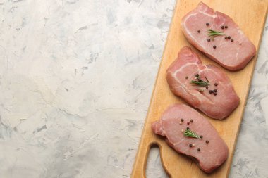 Tahtada çiğ domuz biftek, et ve pişirme için malzemeler, baharat otlar ve hafif bir arka plan üzerinde sebze. üst görünüm. metin için alan