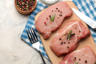 Tahtada çiğ domuz biftek, et ve pişirme için malzemeler, baharat otlar ve hafif bir arka plan üzerinde sebze. üst görünüm.