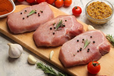 Tahtada çiğ domuz biftek, et ve pişirme için malzemeler, baharat otlar ve hafif bir arka plan üzerinde sebze. Close