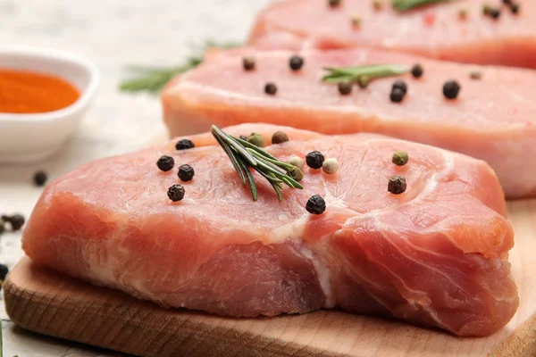 Tahtada çiğ domuz biftek, et ve pişirme için malzemeler, baharat otlar ve hafif bir arka plan üzerinde sebze. Close