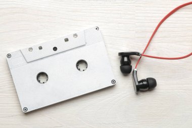 Beyaz ahşap arka plan üzerinde küçük kırmızı-siyah kulaklık ve ses kaseti. üst görünüm