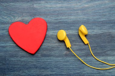 Küçük sarı kulaklıklar ve mavi ahşap arka plan üzerinde kırmızı dekoratif kalp. üst görünüm