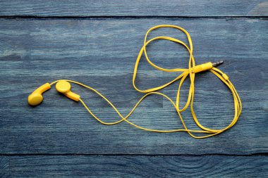 Mavi ahşap arka plan üzerinde akıllı telefon için küçük sarı kulaklıklar. üst görünüm. boş alan