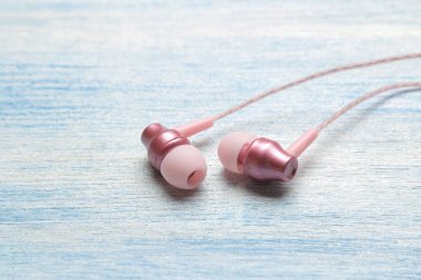 Açık mavi ahşap arka plan üzerinde küçük pembe kulaklıklar. Close