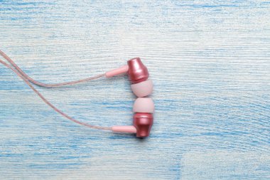 Açık mavi ahşap arka plan üzerinde küçük pembe kulaklıklar. yukarıdan görünüm