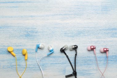 Açık mavi ahşap arka plan üzerinde küçük çeşitli çok renkli kulaklıklar. üst görünüm