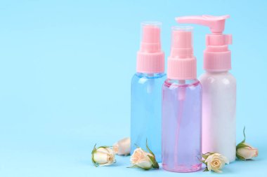 Yumuşak mavi arka plan üzerinde taze gül ile pembe şişelerde yüz ve vücut için Kozmetik. kremler ve losyon. Spa.