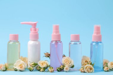 Yumuşak mavi arka plan üzerinde taze gül ile pembe şişelerde yüz ve vücut için Kozmetik. kremler ve losyon. Spa.