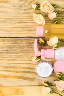 Doğal ahşap arka plan üzerinde taze gül ile pembe şişelerde yüz ve vücut kozmetik. kremler ve losyon. Spa. üst görünüm. metniniz için alan