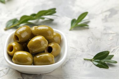 Açık beton arka plan üzerinde yaprakları ile beyaz bir seramik kase yeşil zeytin. Close