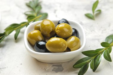 Açık beton arka plan üzerinde yaprakları ile beyaz bir seramik kase yeşil ve siyah zeytin. Close