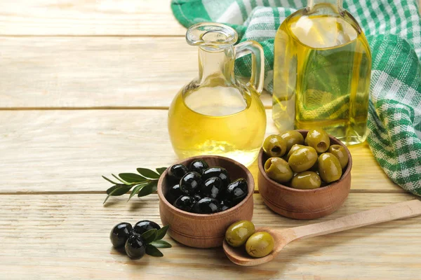 Green and black olives in a wooden bowl with leaves and olive oil on a natural wooden table.
