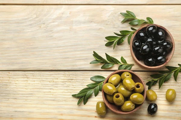 Green and black olives in a wooden bowl with leaves on a natural wooden table. top view. space for text