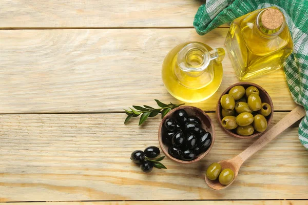Green and black olives in a wooden bowl with leaves and olive oil on a natural wooden table. top view.