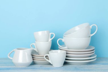 Yumuşak mavi bir arka plan üzerinde beyaz seramik sofra, tabak ve bardak yığınları. Mutfak.