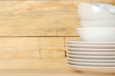 Doğal ahşap arka plan üzerinde beyaz seramik sofra, tabak, tabak ve bardak yığınları. Mutfak.