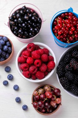 Bir kapta lezzetli çilek, kuş üzümü, böğürtlen, yaban mersini, beyaz ahşap masada ahududu. üst görünüm