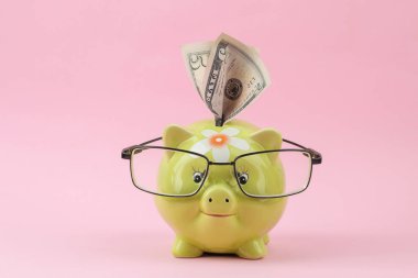 Parlak pembe bir arka plan üzerinde gözlük ve para ile yeşil kumbara. Finans, tasarruf, para. 
