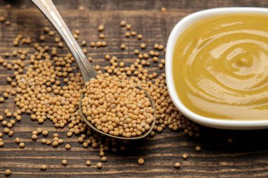 Mustard. mustard sauce in a bowl and dry mustard seeds on a brown wooden table. close-up clipart
