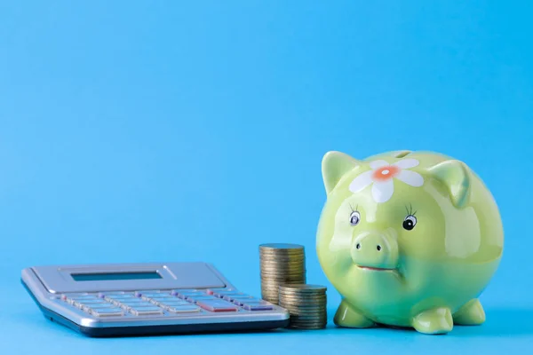 Green pig moneybox and calculator and money on a bright blue background. Finance, savings, money. space for text