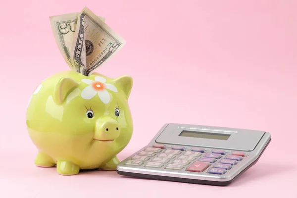 Green pig moneybox and calculator and money on a bright pink background. Finance, savings, money. place for text.