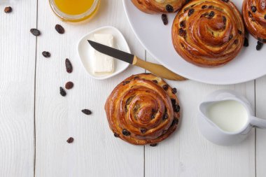 Beyaz ahşap bir masada kuru üzüm ve tereyağı, süt, bal ile lezzetli çörekler. taze fırın. Kahvaltı. Ekmek. üst görünüm