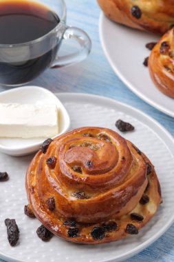 Açık mavi ahşap masada kuru üzüm ve tereyağı ve kahve ile lezzetli çörekler. taze fırın. Kahvaltı. Ekmek.