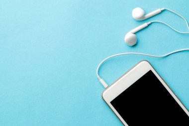 Smartphone. Parlak açık mavi arka planda beyaz telefon ve kulaklıklar. üst görünüm. metin için alan