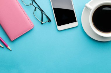 Smartphone. Beyaz telefon, bir fincan kahve ve parlak açık mavi arka plan üzerinde gözlüklü bir dizüstü bilgisayar. üst görünüm.
