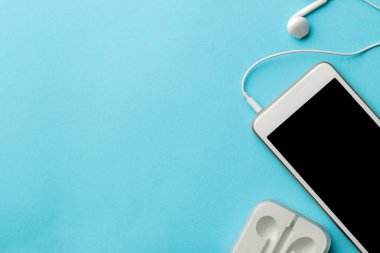 Smartphone. Parlak açık mavi arka planda beyaz telefon ve kulaklıklar. üst görünüm. metin için alan