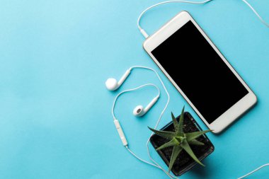 Smartphone. Beyaz telefon ve kulaklıklar ve parlak açık mavi arka plan üzerinde bir çiçek. üst görünüm. metin için alan