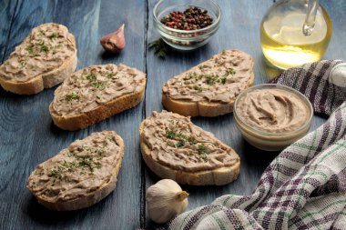 Mavi ahşap bir masada ekmek üzerinde otlar ile taze ev yapımı tavuk ciğeri pate. Bir sandviç.