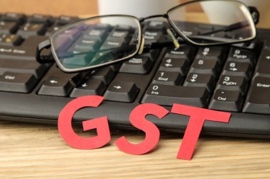 Kağıt harflerden, klavyeden ve doğal ahşap masadaki gözlüklerden Gst kelimesi. Vergi