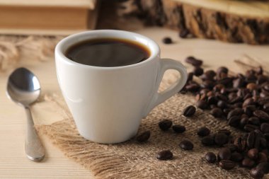 Doğal ahşap bir masada beyaz bir fincan ve kavrulmuş kahve taneleri kahve. Robusta, Arabica